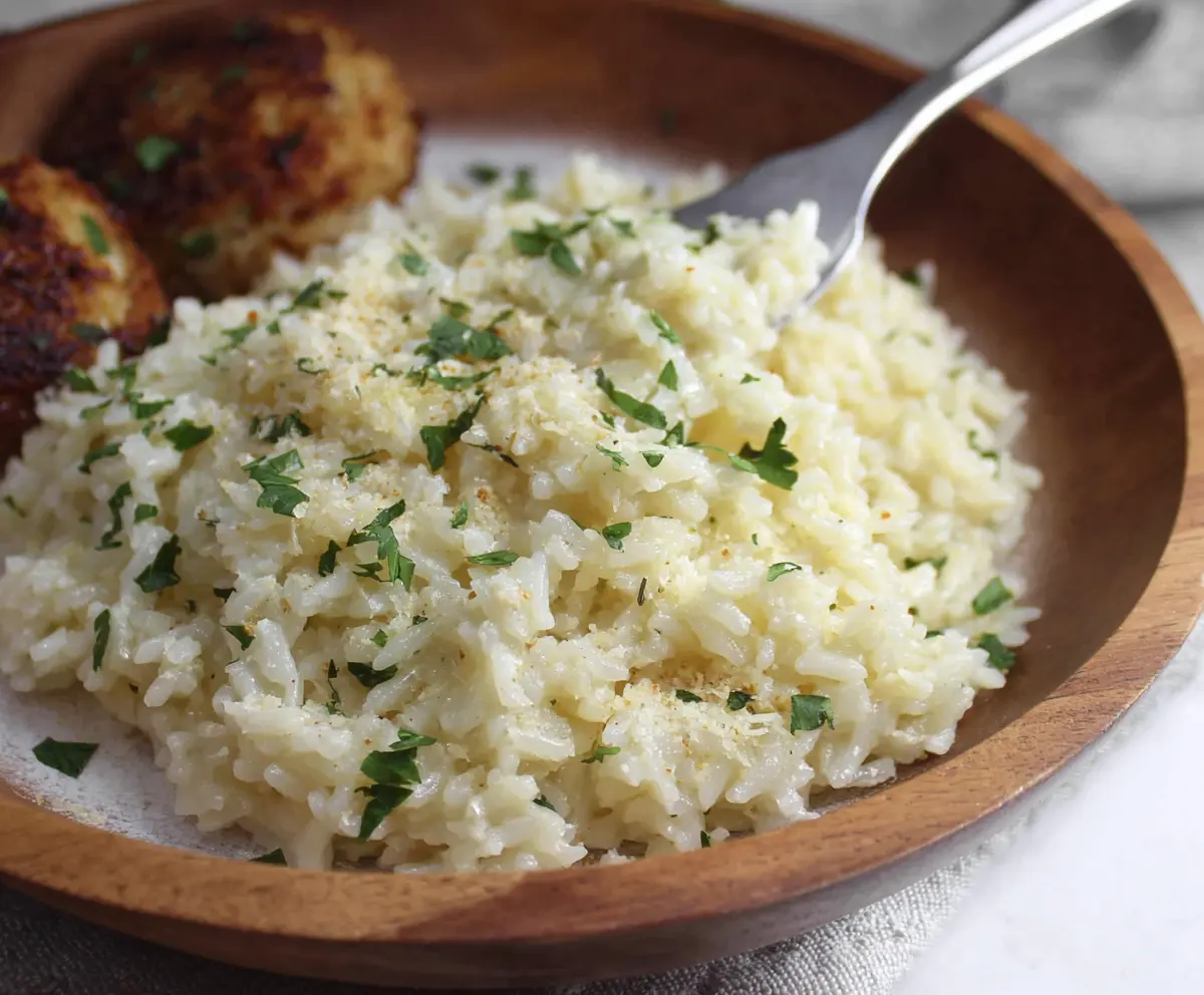 Delicious garlic parmesan rice garnished with fresh herbs, in a white bowl on a rustic wooden table.