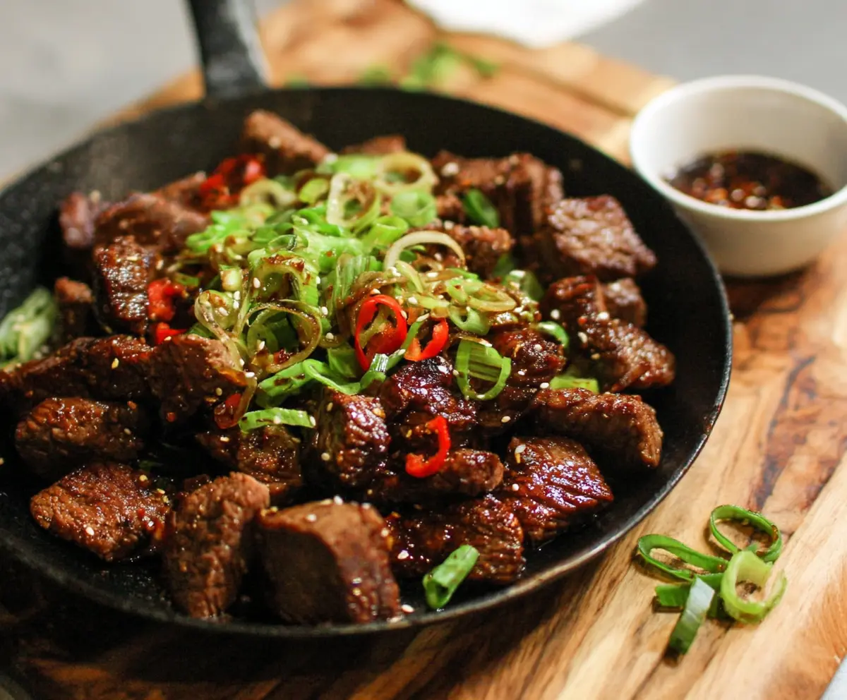 Delicious Korean steak bites garnished with sesame seeds and green onions on a white plate.